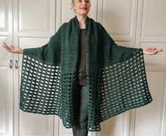 a woman wearing a green crocheted shawl standing in front of white cupboards