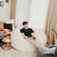 a young man sitting on a bean bag chair in a living room with his legs crossed