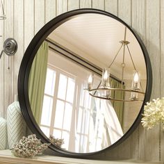 a large round mirror sitting on top of a mantle next to a vase with flowers