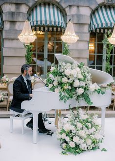 a man sitting at a white piano with flowers on it