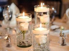 three candles are sitting in glass vases on a table with silverware and napkins