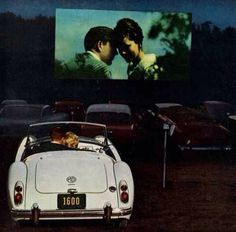 an old photo of two people in a convertible car watching a movie on the screen