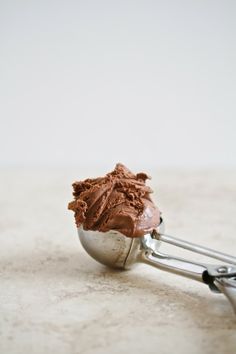 a scoop of chocolate ice cream sitting on top of a metal spoon with tongs