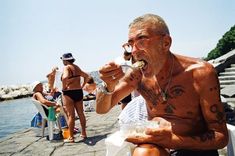 an older man eating food by the water