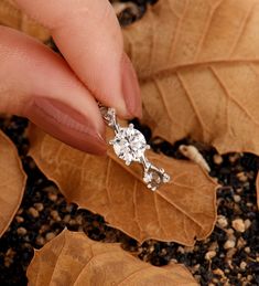 a woman's hand holding onto a diamond ring on top of leaves and gravel