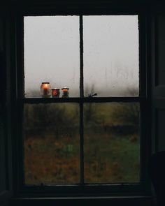 two candles are sitting on the window sill in front of it, with rain coming down