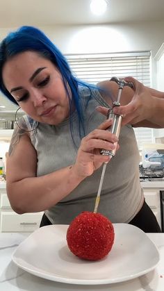 a woman with blue hair is cutting into a red apple on a white platter