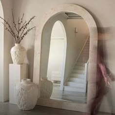 a large white vase sitting on top of a table next to a mirror and stairs