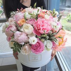 a woman holding a large bouquet of pink and white flowers in front of a window