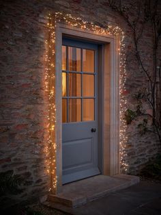 an open door is lit up with fairy lights on the side of a brick building