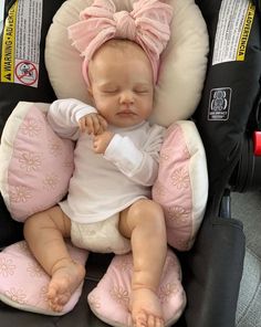 a baby in a car seat with a pink bow on it's head and eyes closed