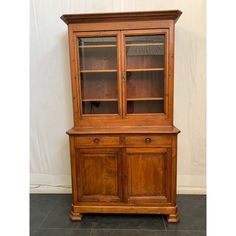 an old wooden china cabinet with glass doors and drawers on one side, in front of a white wall