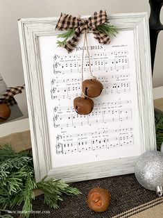 a framed music sheet with three bells hanging from it's side and christmas decorations around the edges