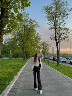 a woman standing on the sidewalk in front of some trees