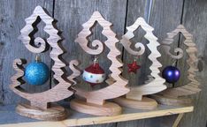 three wooden christmas trees with ornaments hanging from them on a shelf next to a fence