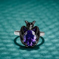 Give wings to your night, make your style with this bat ring that is both fashionable and cool. Crafted in sterling silver, this ring shows a little black bat hugging an oval-cut purple stone with its wings. The bat flying in the dark symbolizes wisdom and courage. This black bat ring is like an elf on your finger, full of mystery. It's a special gift to her as halloween jewelry or vampire bat jewelry worn on halloween or any party.Carat Weight: 3 ctStone Size: 8*10 mmStone Type: Jeulia® StoneNu Bat Ring Jewelry, Vampiric Jewelry, Purple Rings Engagement, Bat Ring, Bat Jewelry, Bat Flying, Purple Rings, Vampire Bat, Purple Jewelry