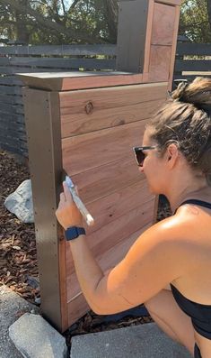 a woman sitting on the ground painting a wooden fence