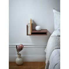 a shelf with books on it next to a flower vase and other items in front of a bed