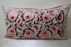 a pink and brown decorative pillow sitting on top of a white bed sheet with an intricate design