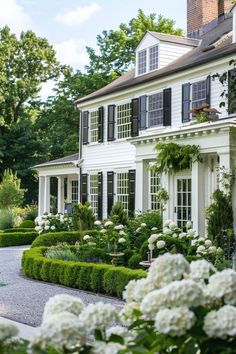 a large white house with lots of windows and plants in the front yard, surrounded by hedges