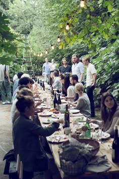 a group of people sitting around a table eating food and drinking wine in the woods