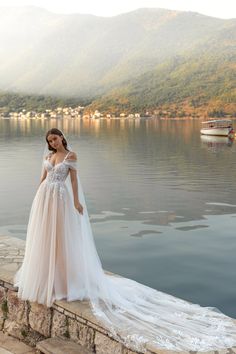 a woman in a wedding dress standing on the edge of a cliff overlooking a body of water