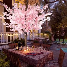 an outdoor dining table set for two with pink flowers on the tree in the center