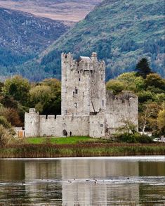 an old castle sitting on top of a lush green hillside next to a body of water