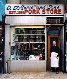 a man standing in front of a store with an apron on his hands and the door open