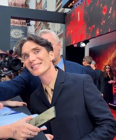 a man in a suit signing autographs for fans on the red carpet at an event