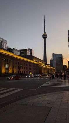 people are walking on the street in front of some tall buildings at dusk with traffic lights