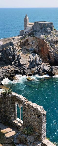 an old stone building sitting on top of a rocky cliff next to the ocean with blue water