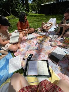 people are sitting on the grass reading books and eating food at an outdoor picnic area