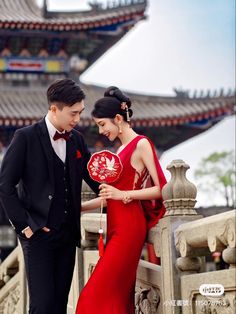 a man and woman in formal wear standing next to each other holding a red fan