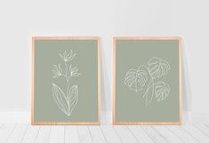 two framed pictures with plants on them against a white wall, one is green and the other is gray