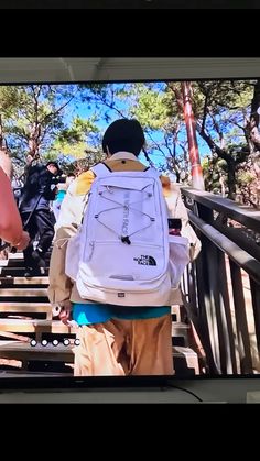 a man with a white backpack walking across a wooden bridge in front of a tv screen