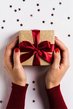 two hands holding a wrapped present box with red ribbon and stars on the wall behind it