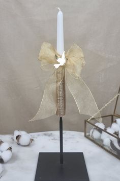 a white candle with a bow on it sitting on a table next to cotton balls