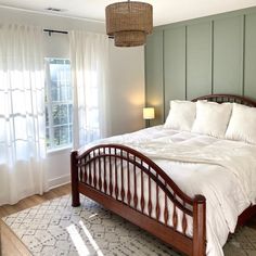 a bed with white sheets and pillows in a bedroom next to a window, rug and lamp