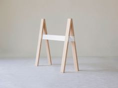 a white chair sitting on top of a floor next to a wooden structure with two legs