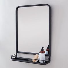 a bathroom mirror and shelf with soap, lotion and hair brush on it in front of a white wall