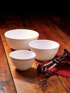 three white bowls sitting on top of a wooden floor next to a pair of scissors