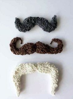 three crocheted mustaches are arranged on a white surface