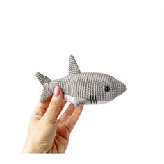 a hand holding a gray knitted shark toy in it's right hand, against a white background