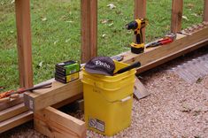 a yellow bucket with tools on it sitting next to a wooden fence in the grass