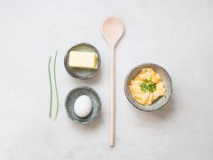 an assortment of food in bowls and spoons on a white surface with a wooden utensil