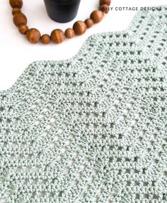 a crocheted blanket next to a beaded necklace and wooden beads on a white surface