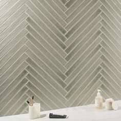 a white table with some pens and bottles on it next to a wall that has grey chevron tiles