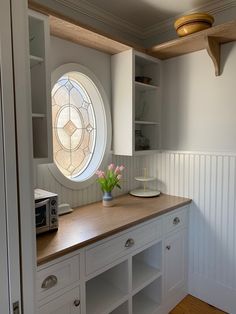 a kitchen with white cupboards and a round window in the wall next to it