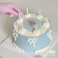 a person in pink gloves is lighting candles on a blue cake with white frosting